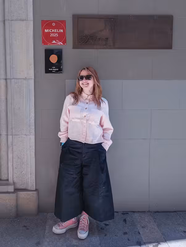 A leadership coach standing outside a restaurant wearing a pink shirt, black trousers and sunglasses